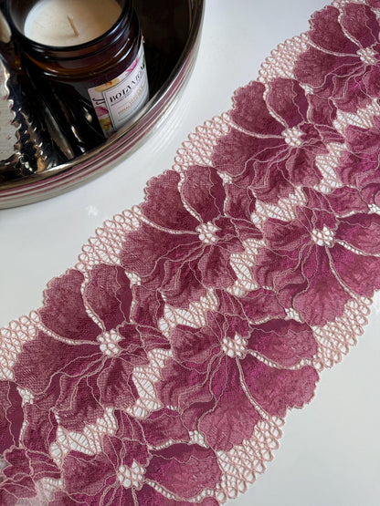 May include: Close-up of a rose pink floral lace trim with a scalloped edge. The lace features large, detailed flower patterns with a delicate, openwork design. The trim is likely used for sewing, crafting, or adding a decorative touch to garments or home decor.