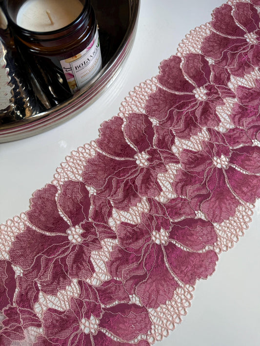 May include: Close-up of a rose pink floral lace trim with a scalloped edge. The lace features large, detailed flower patterns with a delicate, openwork design. The trim is likely used for sewing, crafting, or adding a decorative touch to garments or home decor.